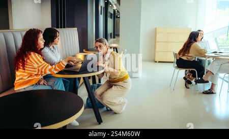 A senior female educator guides students in a bright, modern learning space. The scene emphasizes collaboration, technology, and interactive education Stock Photo