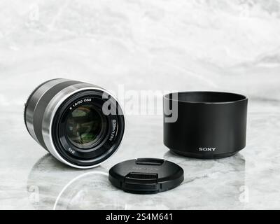 Sony E 50 mm f/1.8 OSS Silver (SEL50F18) lens with front cap removed and lens hood on polished marble surface Stock Photo