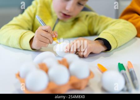 Caucasian child painting white eggs with yellow marker, preparing for easter celebration Stock Photo