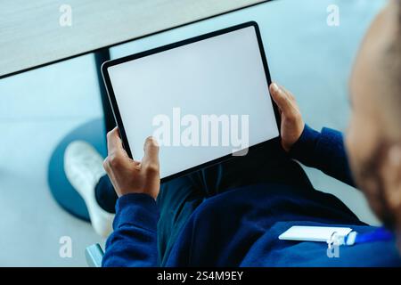 A person sits comfortably holding a tablet with a blank screen, offering ample copy space for customization. The setting is casual, with a hand grippi Stock Photo