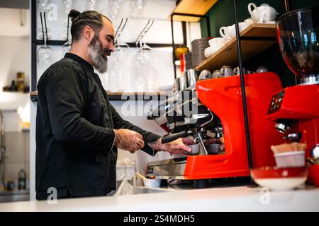 Professional barista in black apron working in restaurant. Portrait of happy barmen who is making coffee in his bar. Stock Photo