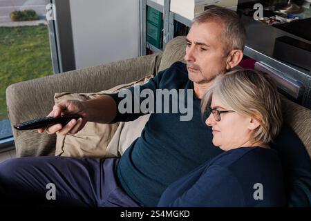 Senior couple relaxing on a comfortable sofa, enjoying a moment together while watching television The serene atmosphere emphasizes warmth and compani Stock Photo