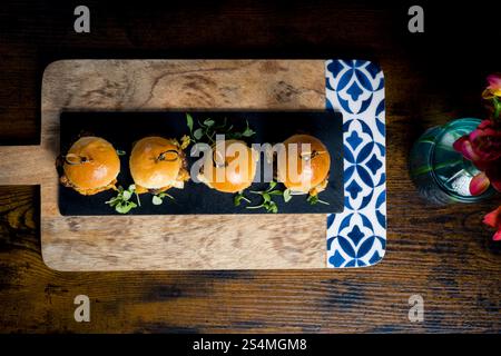 Top-down view of four gourmet pulled pork and cabbage mini burgers served on a black slate board with fresh greens, arranged over a rustic wooden tray Stock Photo