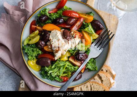 Top view of a nutritious salad featuring raw Kale leaves, multi-colored cherry tomatoes, sliced red onions, BBQ-flavored olives, and spiced feta chees Stock Photo