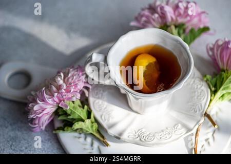 Elegant autumn-themed setup featuring a hot beverage with a lemon slice in a white cup Surrounded by delicate pink chrysanthemums on a rustic surface Stock Photo