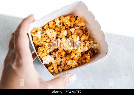 Cropped unrecognizable person in a close-up shot from above, holding a box filled with sweet caramel popcorn. Stock Photo