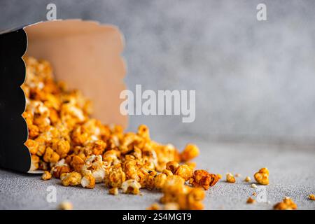 Caramel popcorn tumbling out of a black carton onto a textured gray background. Stock Photo