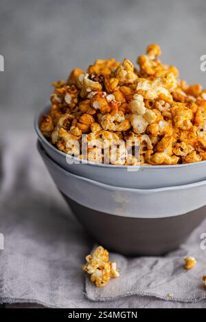 Gray bowl filled with crunchy, sweet caramel popcorn, placed on a soft-textured gray cloth. Stock Photo