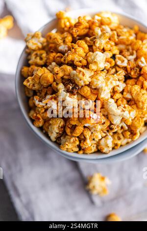 Top view of a bowl filled with crunchy caramel popcorn on a textured cloth background. Stock Photo