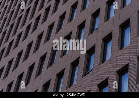 A detailed view of a modern building facade featuring a repetitive geometric pattern with aligned windows set in dark, textured cladding. This archite Stock Photo