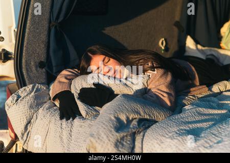 A young Latina woman sleeps soundly, wrapped in a cozy blanket in a van while camping in Iceland. The scene captures a tranquil and serene moment as t Stock Photo