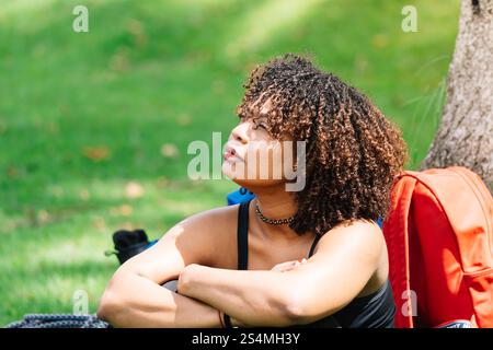 A Black woman sits under a tree in a Bogota park, resting her arms on her knees while gazing into the distance Surrounded by greenery, she appears ref Stock Photo