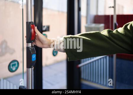 A woman in a green coat presses a red button on a pole of a city bus The scene shows the daily commute to work in an urban environment illuminated by Stock Photo