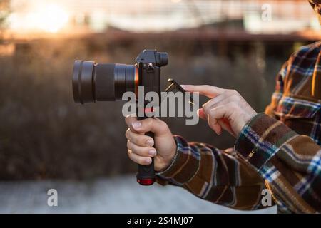 Close-up of hands holding a camera and adjusting the screen during golden hour The scene captures the soft lighting of the sunset, highlighting the ca Stock Photo