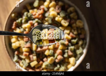 A spoon displaying 2026 in colorful number shaped pasta celebrates the upcoming new year, showcased amidst a bowl of assorted pasta. Stock Photo