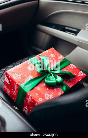 A beautifully wrapped red gift with a green ribbon rests on a car seat, capturing the anticipation of giving during the holiday season Perfect for fes Stock Photo
