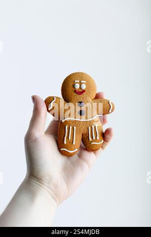 A hand holding a cheerful gingerbread man cookie, decorated with white and red icing, isolated against a clean white background Perfect for holiday or Stock Photo