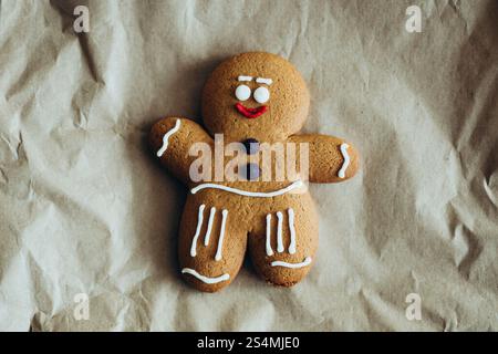 A festive gingerbread man cookie decorated with icing, lying on a crumpled brown paper surface Perfect for holiday themes and Christmas celebrations Stock Photo