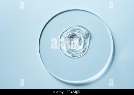 A clear gel with small golden specks on a round glass plate against a light blue background The minimalistic composition highlights texture and transp Stock Photo
