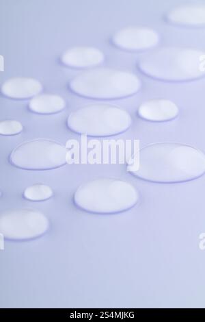 Close-up image of droplets scattered on a smooth, lavender-colored surface The droplets vary in size, creating a calming and serene visual effect Stock Photo