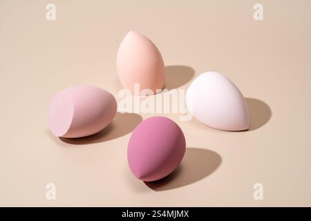 A set of four cosmetic sponges in pink, peach, cream, and mauve shades arranged on a neutral background, perfect for applying foundation and achieving Stock Photo