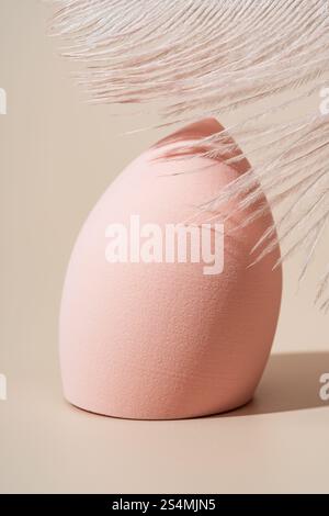 A soft, pink cosmetic sponge displayed with feather details on a beige background Ideal for beauty products, makeup tutorials, and skincare promotions Stock Photo
