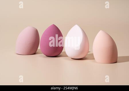 A set of four soft cosmetic sponges in varying pink shades, perfect for makeup application, displayed on a smooth beige surface Ideal for beauty and m Stock Photo