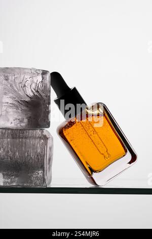 Aesthetic close-up of a vitamin C serum in a clear pipette bottle resting against ice blocks on a glass surface Perfect for skincare and wellness them Stock Photo