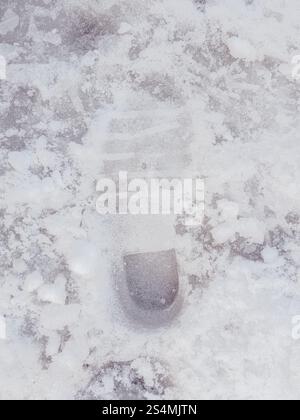 A single shoe imprint is visible on a snow-covered pavement, illustrating a winter scene in a city setting. Stock Photo