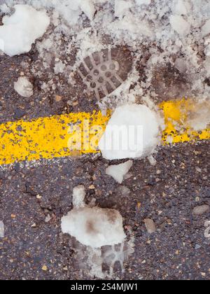 Melting snow reveals a manhole cover by a painted yellow line on gritty urban asphalt, capturing winter's retreat in the city. Stock Photo