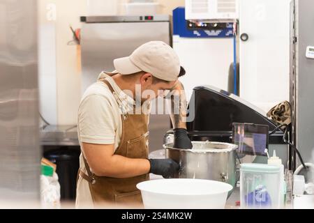 A dedicated baker in a traditional Italian bakery mixes dough in a stainless steel bowl, showcasing the art of bread making The kitchen has various ba Stock Photo
