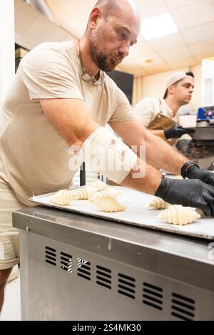 Skilled bakers work in an Italian bakery, preparing dough for fresh pastries The warm, inviting atmosphere of the kitchen highlights the art of tradit Stock Photo