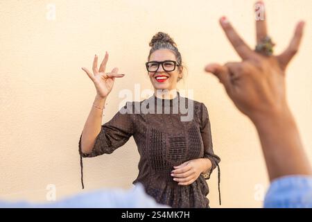 A cheerful instructor in glasses teaches sign language, engaging with a participant in an outdoor setting The close interaction highlights communicati Stock Photo