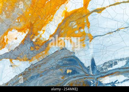 A captivating abstract image showcasing multicolored mud with striking orange, blue, and white hues The cracked textures create an intricate, beautifu Stock Photo