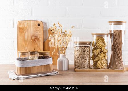 A contemporary kitchen countertop displays wooden cutting boards next to elegant glass jars filled with pasta and grains, accented by a white brick wa Stock Photo