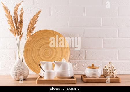 A contemporary kitchen setup displaying ceramic teapots and cups on wooden trays, complemented by dried pampas grass in a textured vase, against a whi Stock Photo