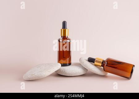 Two amber dropper bottles are artistically arranged on stacked smooth stones against a subtle beige background, creating a balanced and minimalist aes Stock Photo
