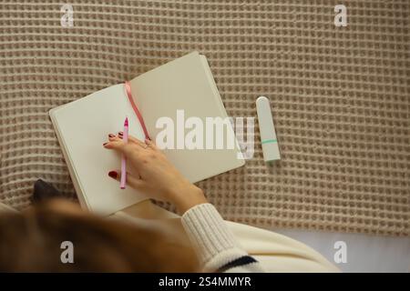 A person holds a pink pen over an open notebook with a marker, placed on a textured beige blanket, creating a cozy atmosphere Ideal for journaling and Stock Photo