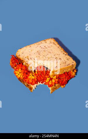 Close-up of a sandwich filled with bright red and yellow flowers against a bold blue background. The mix of food and floral elements creates a unique, Stock Photo
