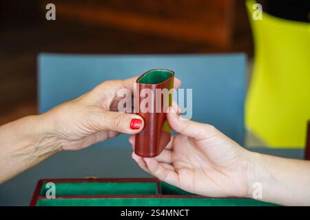 Two hands exchange a brown dice cup during a backgammon game, showcasing a moment of strategy and anticipation The green interior contrasts with the s Stock Photo