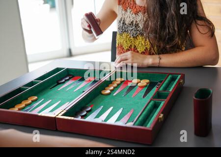 A close-up photo of a backgammon game in progress Two players concentrate on their moves, with checkers and dice on a green board The scene conveys st Stock Photo