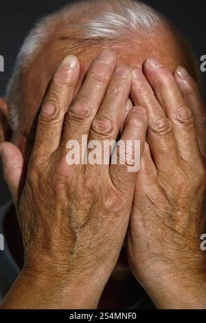 Close-up of a senior man covering his face with age-marked hands in a moment of contemplation Captures the texture of mature skin and expressive gestu Stock Photo