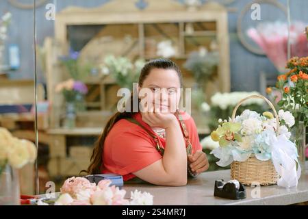 Medium close up portrait of beautiful florist with down syndrome leaning on table while posing for photo Stock Photo