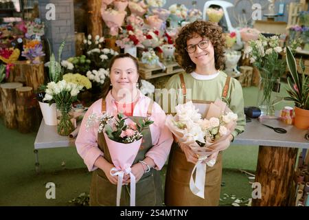 High angle shot of two talented florists standing in center of flower shop and demonstrating bouquets of roses Stock Photo