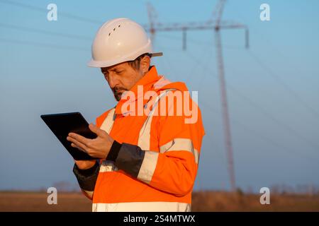 Electrical engineer using digital tablet computer out in the field close to electricity pylons, selective focus Stock Photo