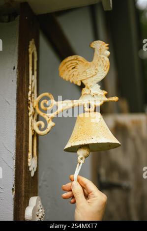 Hand ringing a rustic bell with a rooster design mounted on a barn Stock Photo