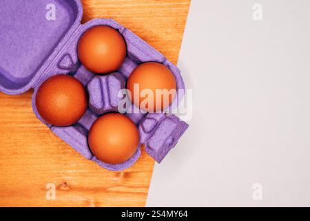 Four chicken eggs in violet cardboard box on the table, top view Stock Photo