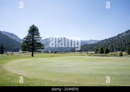 View across a large green on a mountain golf course. The mountains can be seen in the distance, against a blue, summers sky. Stock Photo