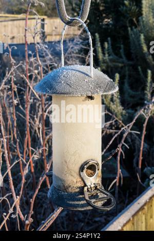 A nearly empty bird feeder on a cold, frosty morning in winter.  Ready to be re-filled with seeds. Stock Photo