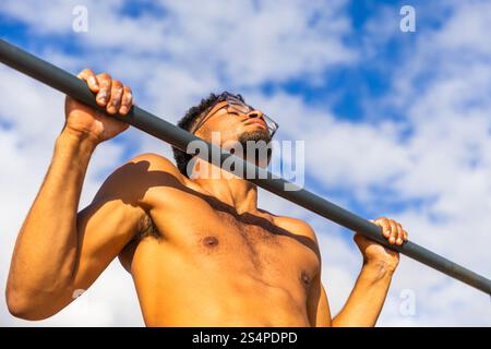A man is doing pull-ups outdoors, fit person training Stock Photo
